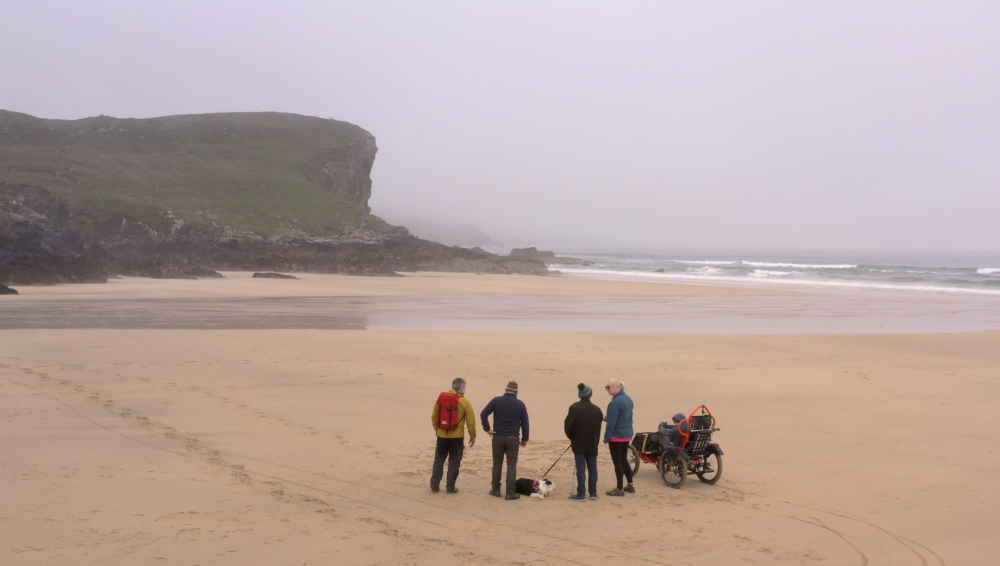 A group of people walking and wheeling on Tolsta Beach in Lewis, Scotland.